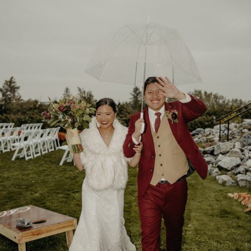 A bride and groom walking with an umbrella